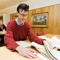 Two individuals engaged in reading archives and collections in the State Library of Tasmania and Tasmanian Archives Reading Room.