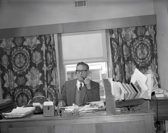 A picture of a man sitting behind a desk smoking from a pipe