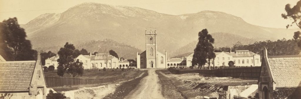 A black and white photo of a road leading to a church building. A mountain in the ddistance.