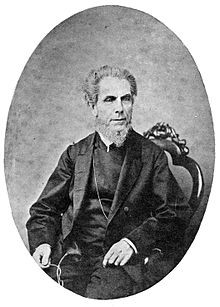 A black and white photo of a man sitting at a chair.